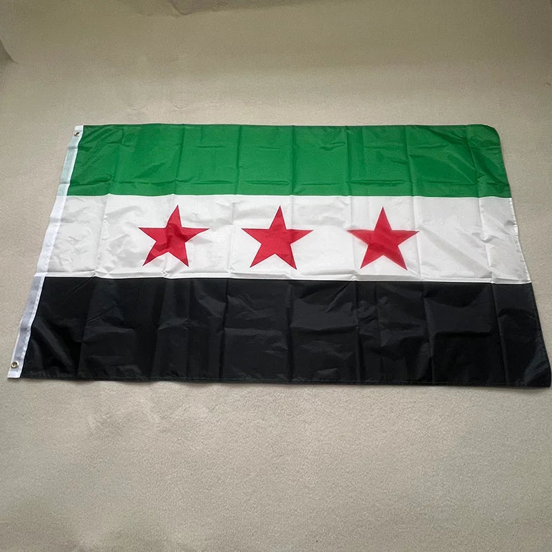 Syrian flag standing firm amid dust and sun, reflecting resistance, heritage, and the unbroken spirit of the Syrian people.
